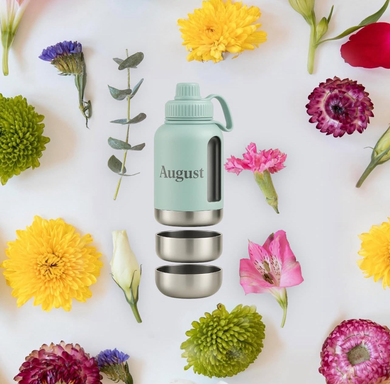 Mint green 'August' water bottle with silver base and lid surrounded by colorful flowers on a white background